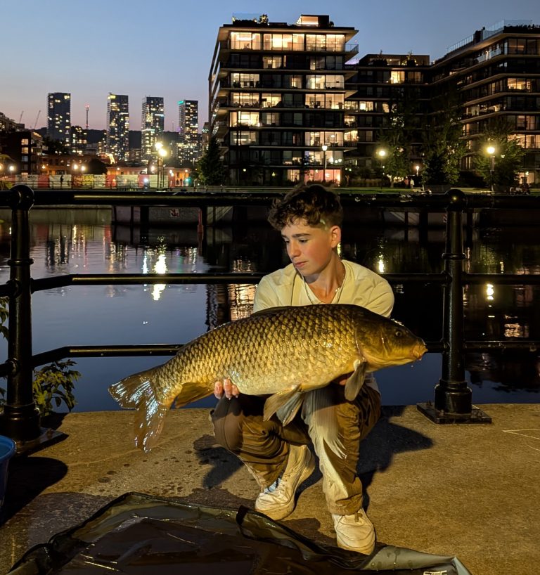 Jeune homme tenant une carpe dans ses mains sur le bord d'un canal en centre-ville