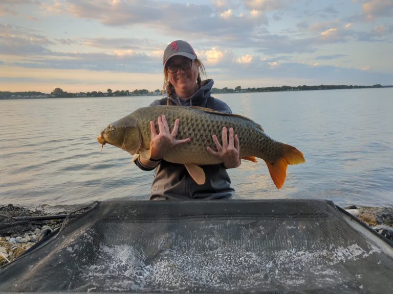 Femme tenant une carpe dans ses bras au bord du fleuve saint-Laurent